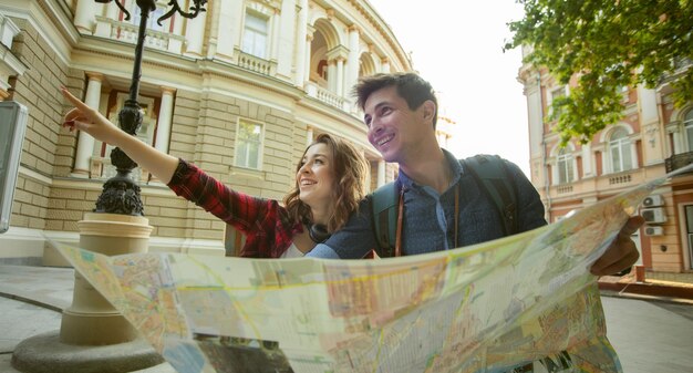 Feliz jovem casal de viajantes segurando um mapa nas mãos enquanto caminhava pela cidade. Conceito de viagem