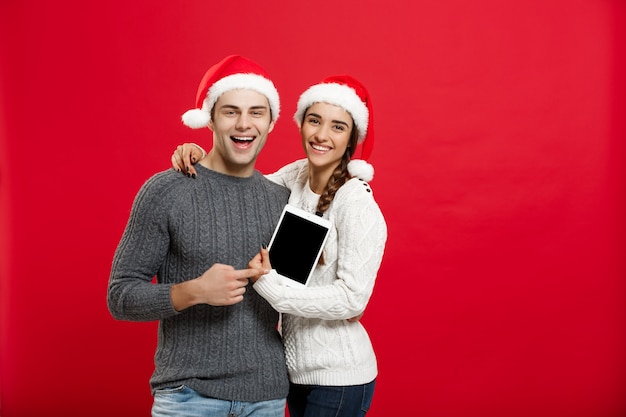 Feliz jovem casal em camisolas de natal com tablet digital.