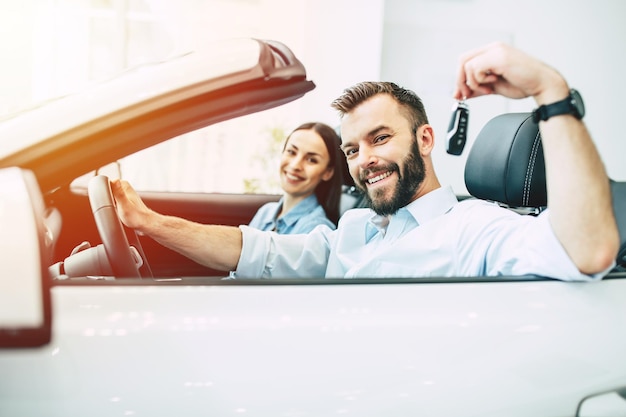 Feliz jovem casal escolhe e compra um carro novo para a família na concessionária