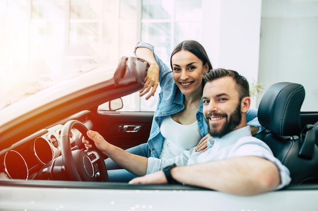 Feliz jovem casal escolhe e compra um carro novo para a família na concessionária