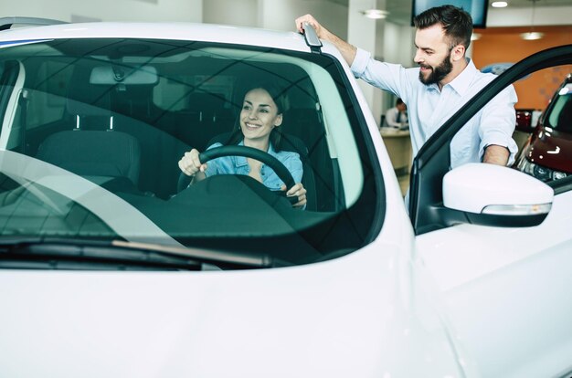 Feliz jovem casal escolhe e compra um carro novo para a família na concessionária