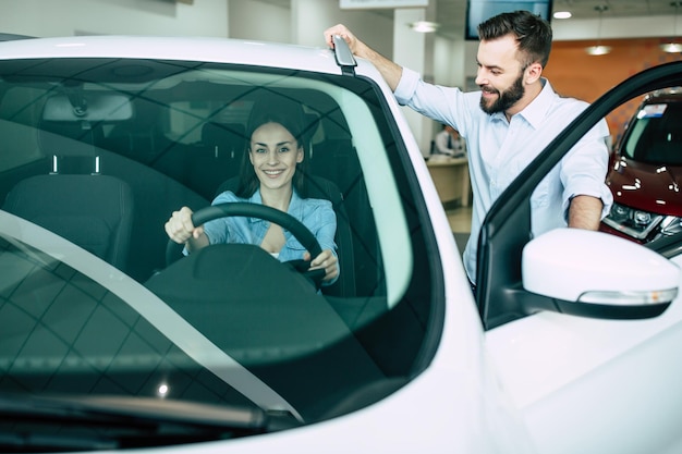 Feliz jovem casal escolhe e compra um carro novo para a família na concessionária