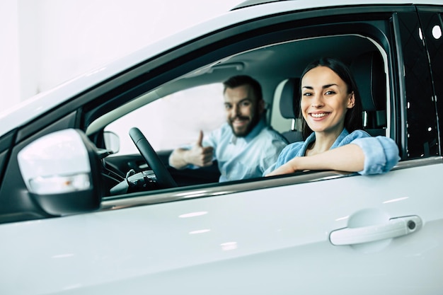 Feliz jovem casal escolhe e compra um carro novo para a família na concessionária