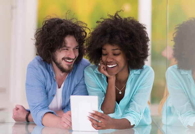 Foto feliz jovem casal multiétnico deitado no chão se divertindo usando tablet digital