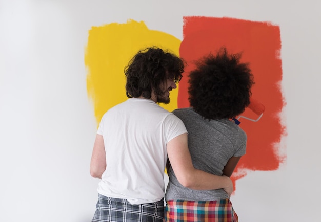 feliz jovem casal multiétnico pintando a parede interior da casa nova