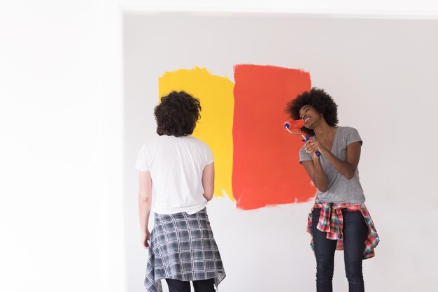 feliz jovem casal multiétnico pintando a parede interior da casa nova