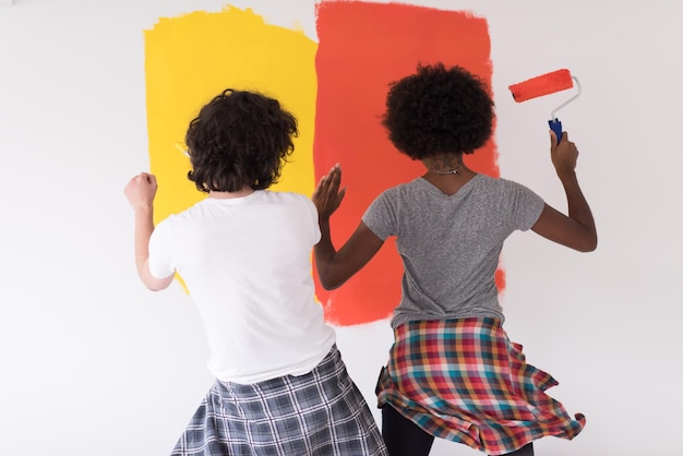 feliz jovem casal multiétnico pintando a parede interior da casa nova