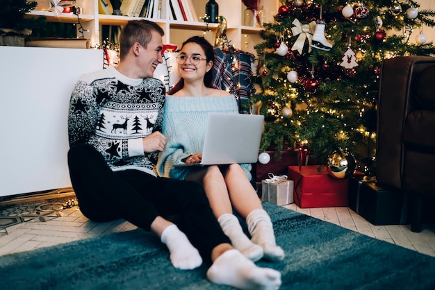 Feliz jovem casal navegando no laptop ao lado da árvore de Natal