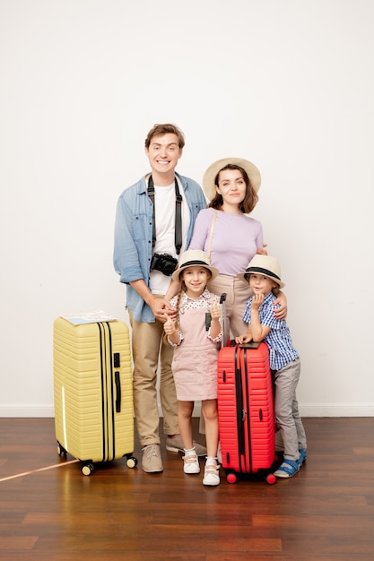 Feliz jovem casual pai, mãe, filho e filha com a bagagem em pé na parede no estúdio, prontos para a viagem