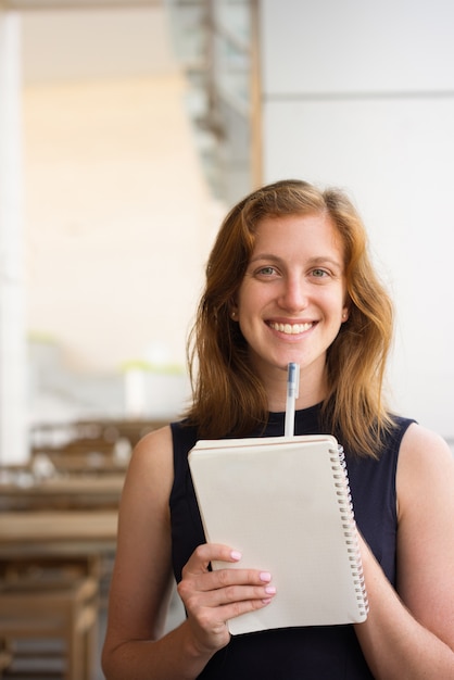 Feliz jovem com caneta e caderno no café