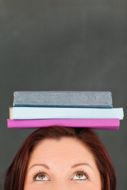 Foto feliz jovem com livros em sua cabeça com a câmera focada no topo da cabeça