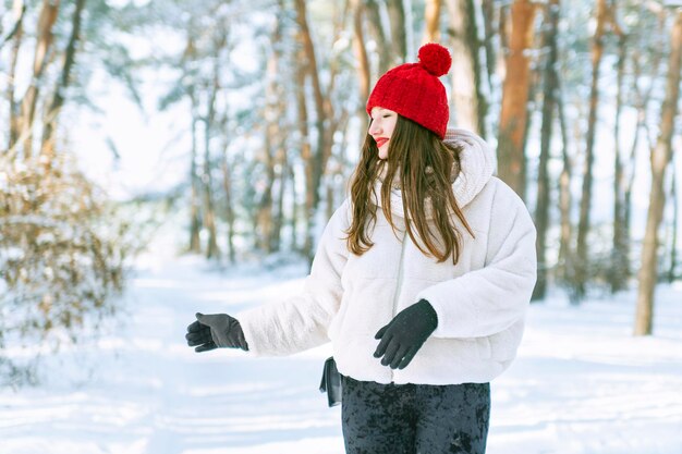 Feliz jovem de chapéu vermelho com olhos fechados aproveitando o momento na floresta nevada Dia ensolarado no parque de inverno