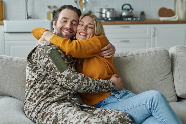 Feliz jovem em forma militar abraçando sua esposa depois de voltar para casa do exército