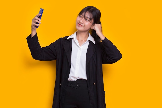 feliz jovem empresária asiática usando telefone celular isolado em fundo amarelo