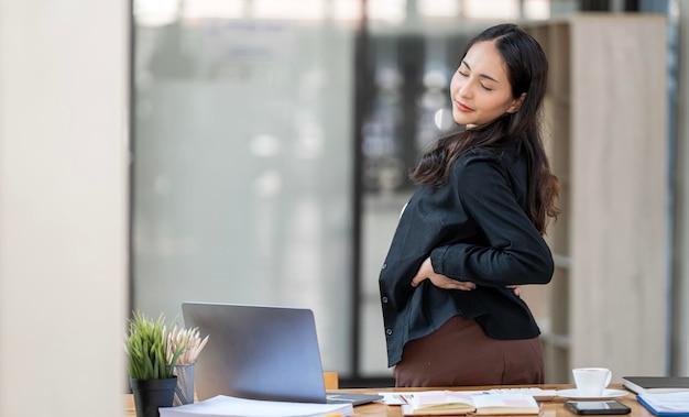 Feliz jovem empresária fazendo alongamento de cintura no escritório sentado na mesa por muito tempo