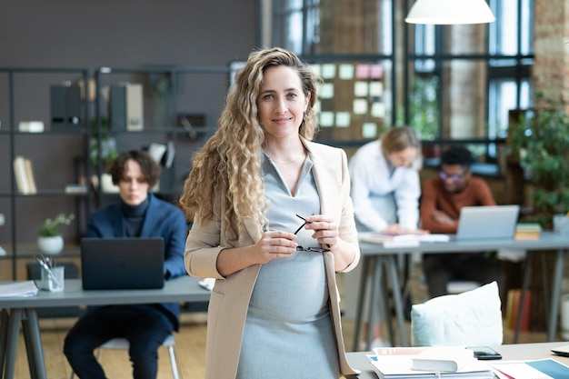 Feliz jovem empresária grávida em trajes formais olhando para você