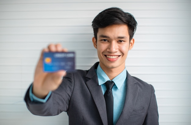 Feliz jovem empresário asiático sorrindo para a câmera e demonstrando o cartão de crédito contra