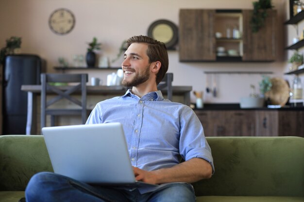 Feliz jovem empresário freelancer sentado no sofá com o laptop, trabalhando remotamente online em casa.