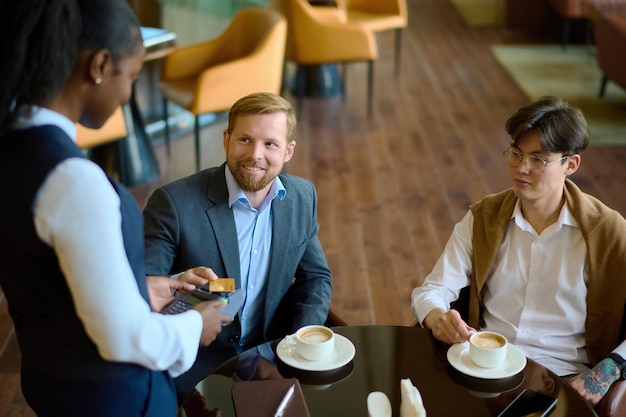 Feliz jovem empresário pagando com cartão de crédito para café no salão do hotel