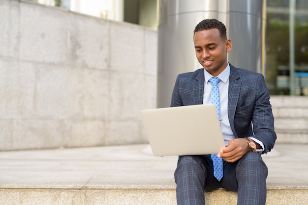 Feliz jovem empresário trabalhando com laptop enquanto está sentado na escada ao ar livre