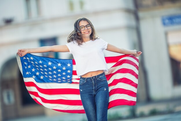 Feliz jovem estudante americana segurando e acenando na cidade com a bandeira do EUA.