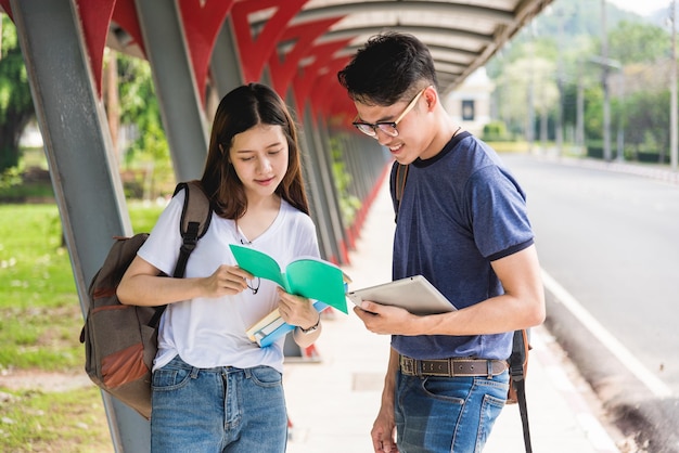 Feliz jovem estudante asiático lendo em computadores tablet no campus. Há grupos de namoradas atrás, Educação de volta ao conceito universitário