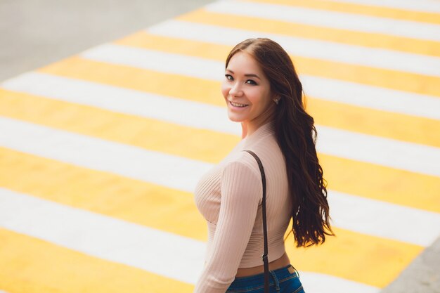 Feliz jovem estudante feminino atravessar a rua e derrubar o chapéu contra a cidade urbana