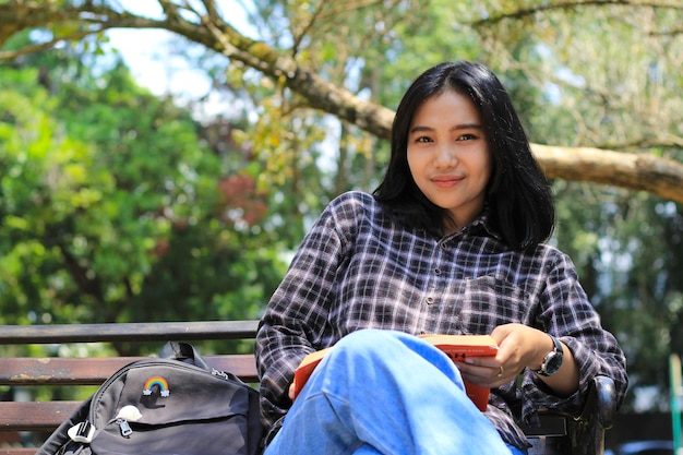 feliz jovem estudante universitária asiática com rosto sorridente gosta de ler um livro para exame no parque