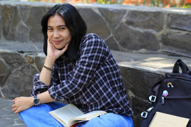 feliz jovem estudante universitária asiática com rosto sorridente gosta de ler um livro para exame no parque
