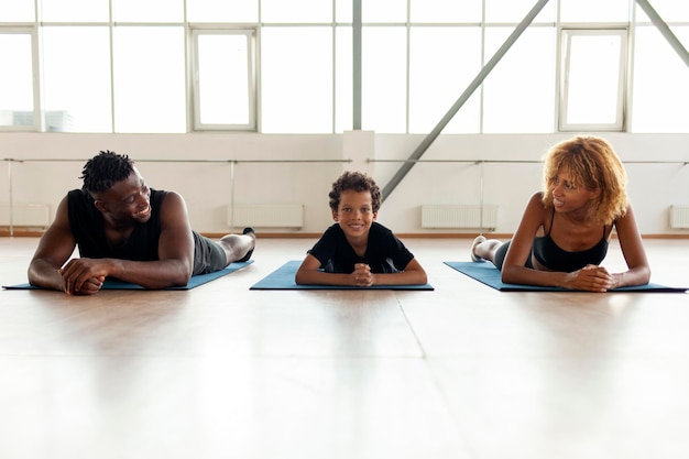 feliz jovem família afro-americana mente e descansa no tapete de ioga na academia mãe pai e filho