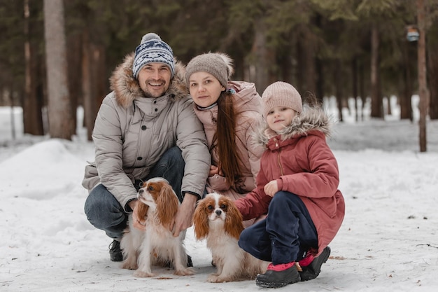 Feliz jovem família caucasiana brinca com um cachorro no inverno em uma floresta de pinheiros