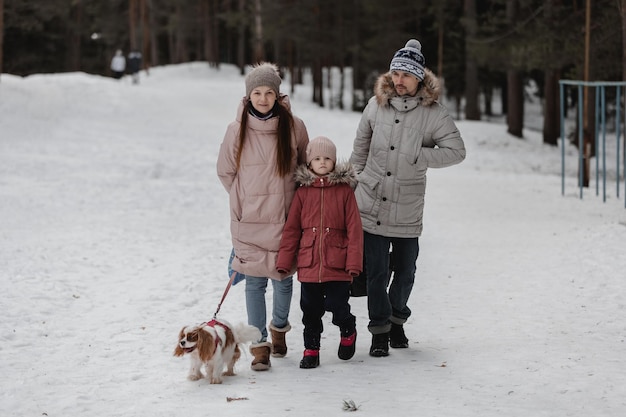 Feliz jovem família caucasiana brinca com um cachorro no inverno em uma floresta de pinheiros