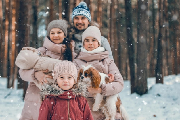 Feliz jovem família caucasiana brinca com um cachorro no inverno em uma floresta de pinheiros