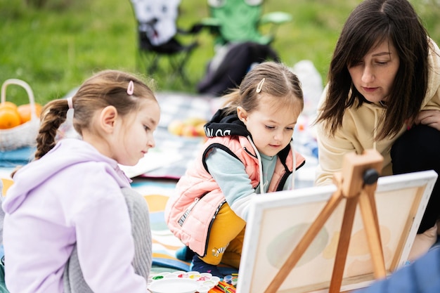 Feliz jovem família mãe e filhas se divertindo e curtindo ao ar livre na pintura de manta de piquenique no relaxamento do jardim primavera