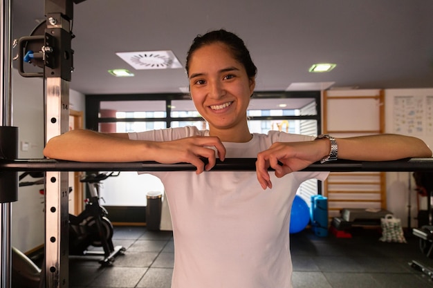 Feliz jovem hispânica apoiando-se em uma barra na academia