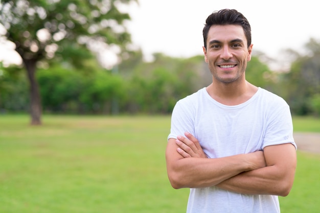 Feliz jovem hispânico sorrindo com os braços cruzados no parque