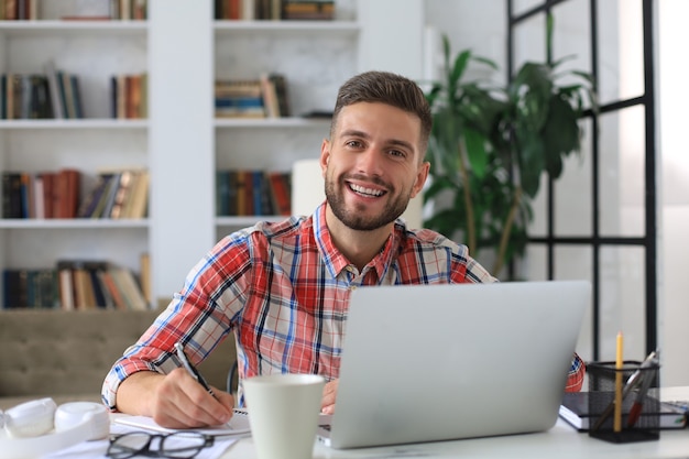 Feliz jovem homem de negócios está analisando documentos financeiros de casa durante o auto-isolamento.