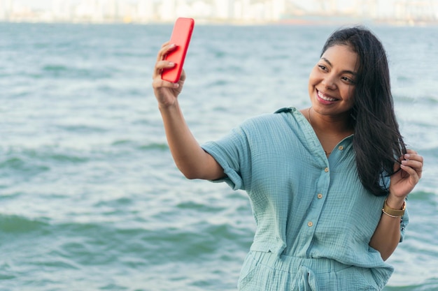 Feliz jovem latina com roupa da moda tirando uma selfie no parque