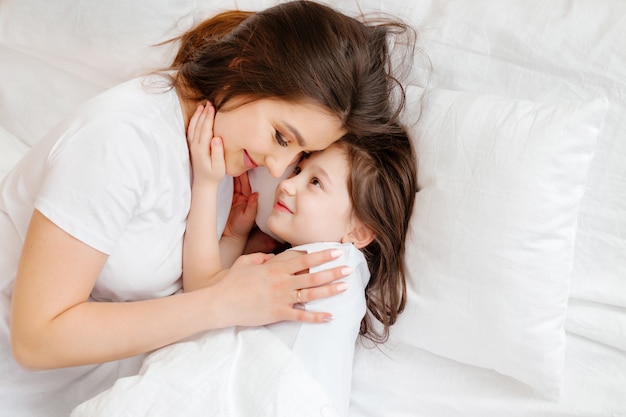 Feliz jovem mãe abraça sua filha na cama