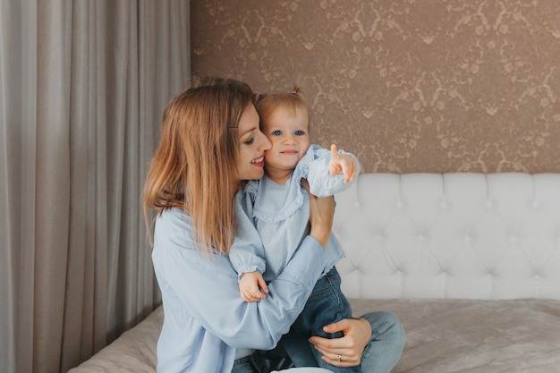 Feliz jovem mãe brinca com a filha na cama em casa. dia das Mães.