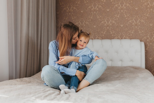 Feliz jovem mãe brinca com a filha na cama em casa. dia das Mães.