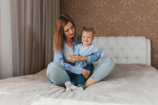 Feliz jovem mãe brinca com a filha na cama em casa. dia das Mães.