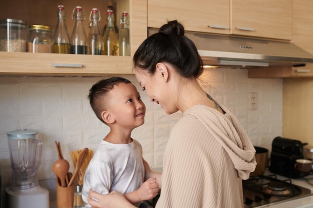 Feliz jovem mãe conversando com o filho sentado no balcão da cozinha