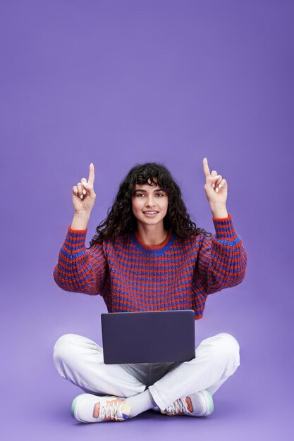 Feliz jovem morena com laptop apontando para cima