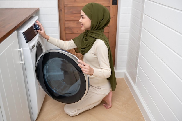 Feliz jovem muçulmana usando hijab lavando roupa no conceito de estilo de vida saudável em casa