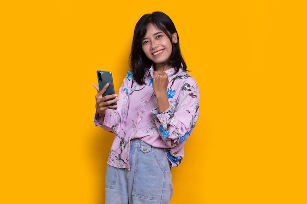 feliz jovem mulher bonita asiática usando telefone celular isolado em fundo amarelo