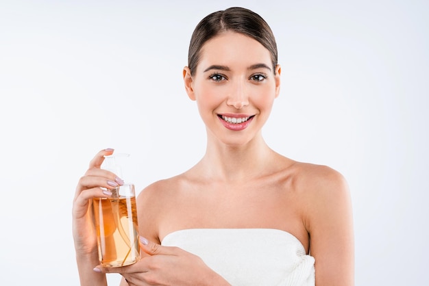 Feliz jovem mulher bonita caucasiana mostrando garrafa cosmética sobre fundo branco