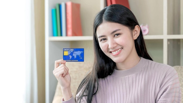 Feliz jovem mulher bonita sentada no sofá na sala de estar em casa ela sorrindo e usa cartão de crédito para fazer compras on-line compras on-line e conceito de banco on-line