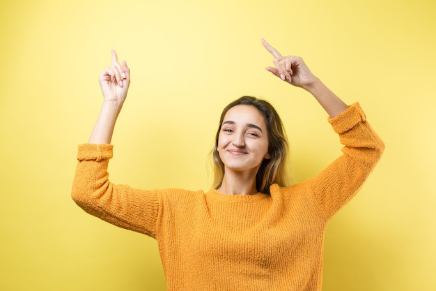 Feliz, jovem mulher caucasiana, com um suéter laranja, levanta o punho cerrado de alegria