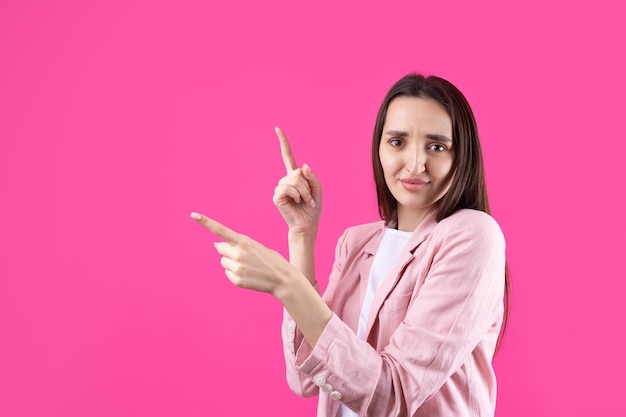 Feliz jovem mulher caucasiana em uma jaqueta rosa apontando os dedos para longe
